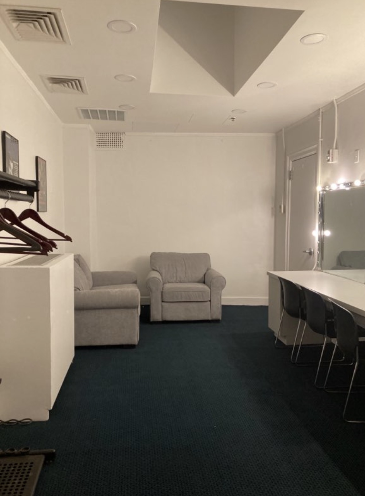 Stage-right dressing room with lounge chairs, garment storage, and illuminated mirror counter